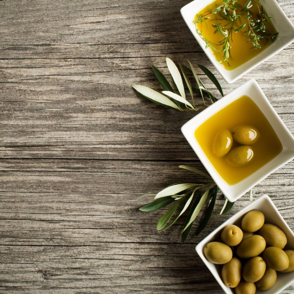 Three small bowls of olive oil varieties lie on a wooden table next to each other.