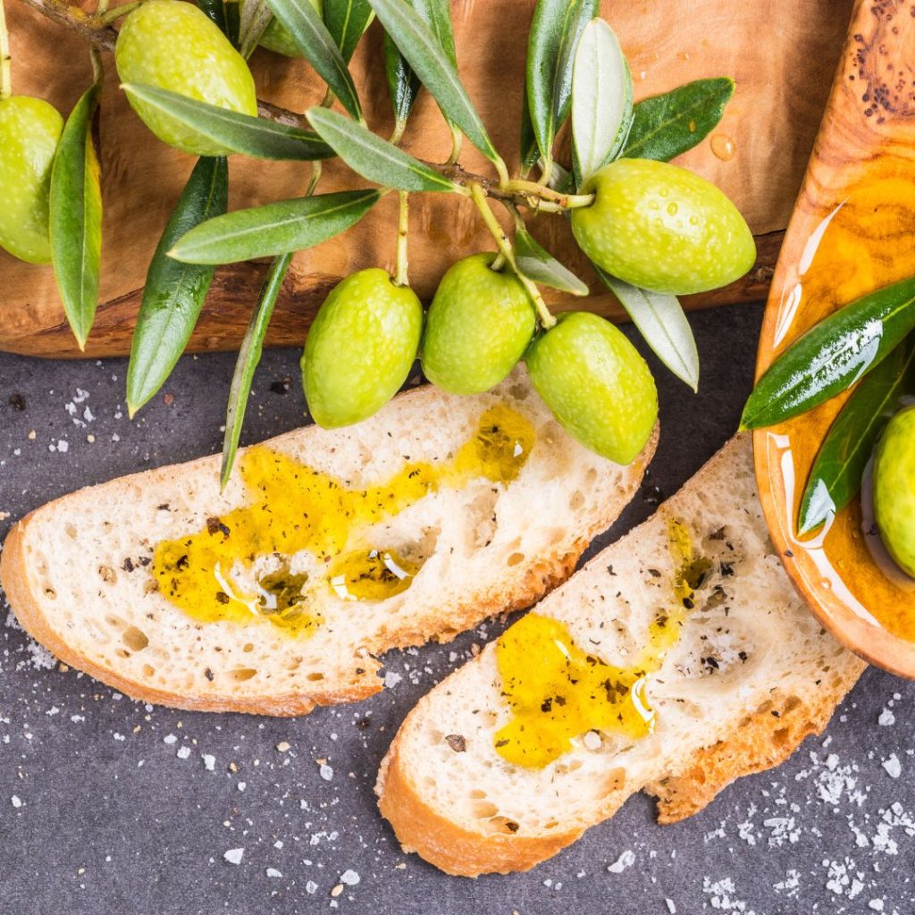 Two loaves of bread lay on the table with freshly picked olives.