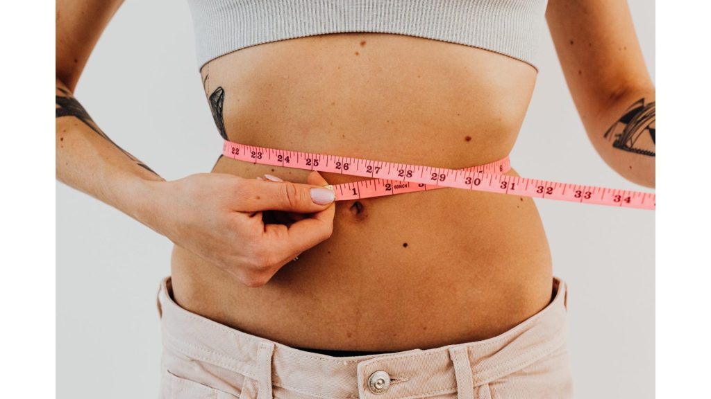 A woman measuring her waist with a measuring tape.