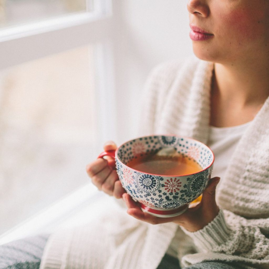 A woman holding a cup of tea in front of a window.