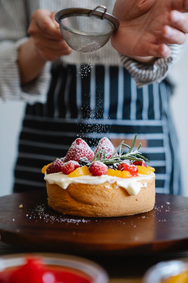 A woman gracefully sprinkles sugar on a cake, enhancing its flavor with the aromatic essence of native vanilla beans.