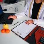 A woman in a lab coat is snacking on wasabi peas while working at her desk.