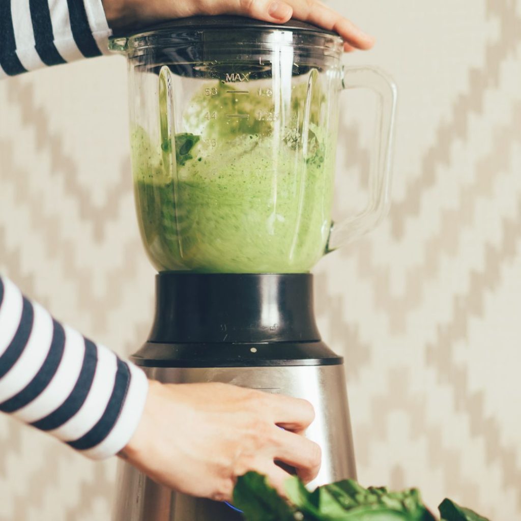 A person blending greens in a Vitamix blender.