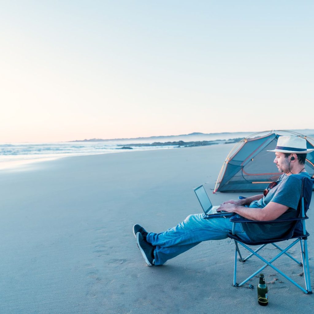 A man enjoying the beach with a camping chair and a laptop.