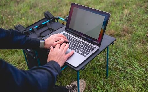 A man using a laptop on a table in the grass.