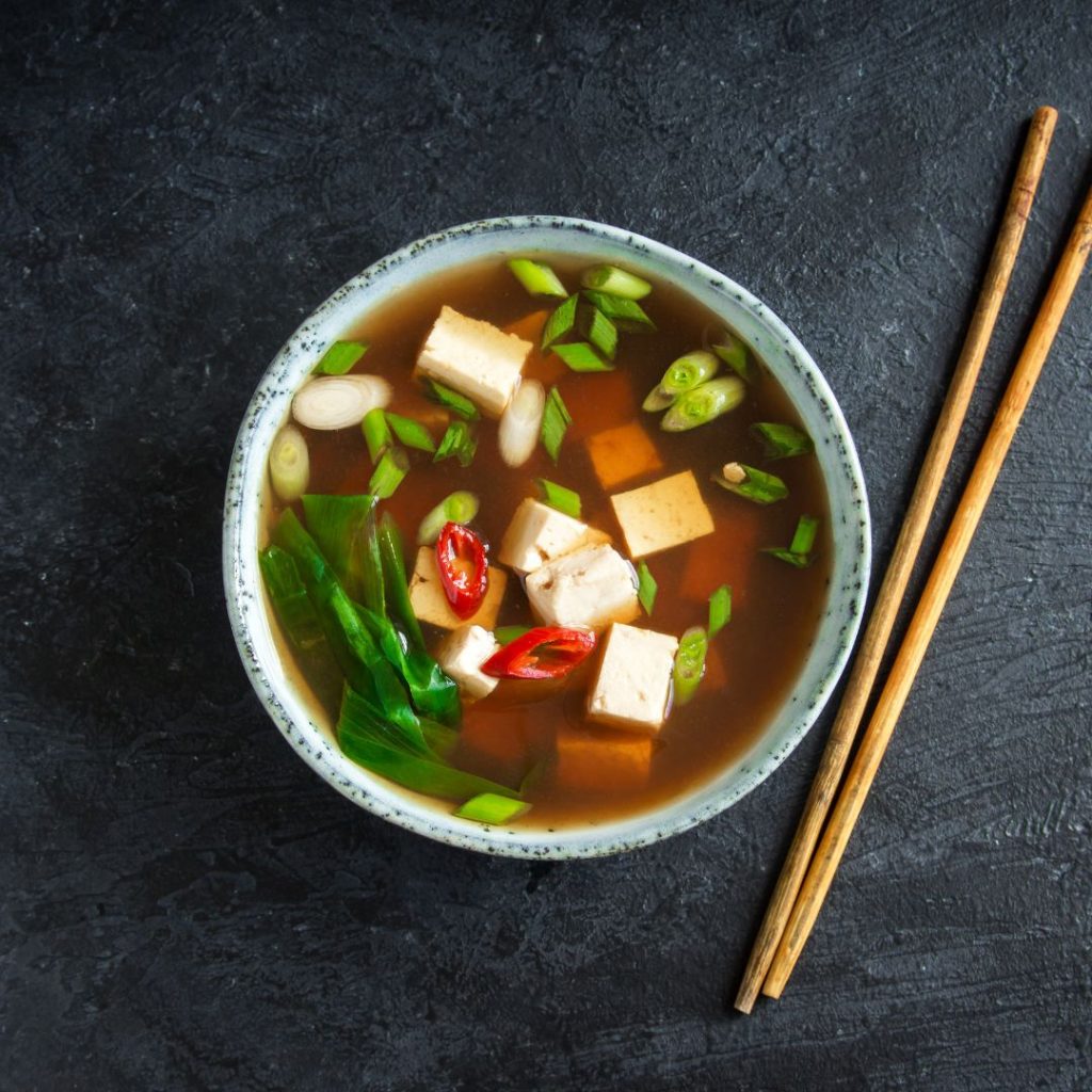 A bowl of miso soup with chopsticks on a dark background.