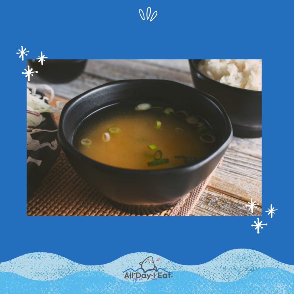 A bowl of miso soup and rice on a blue background.