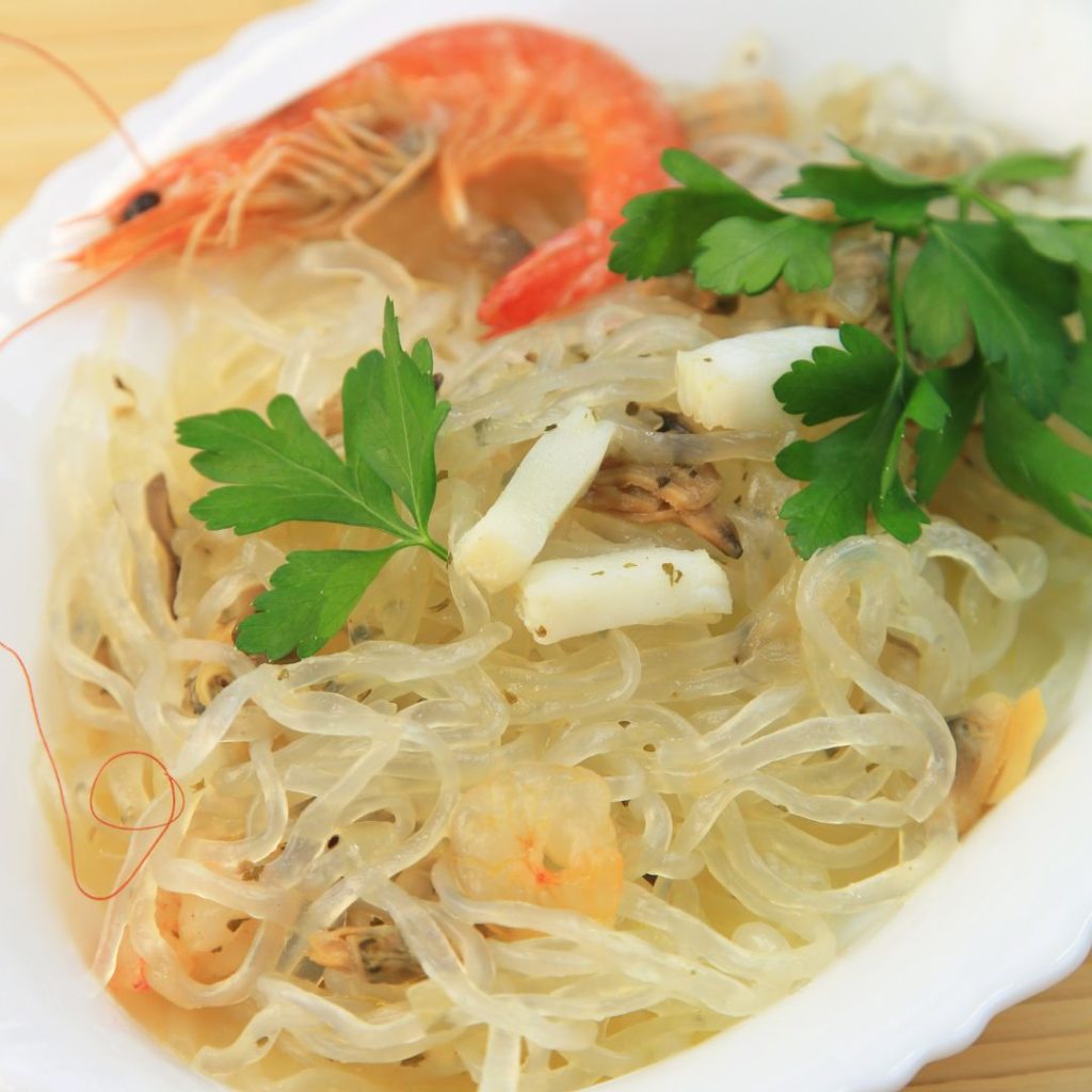 A bowl of white noodles with shrimp and parsley.