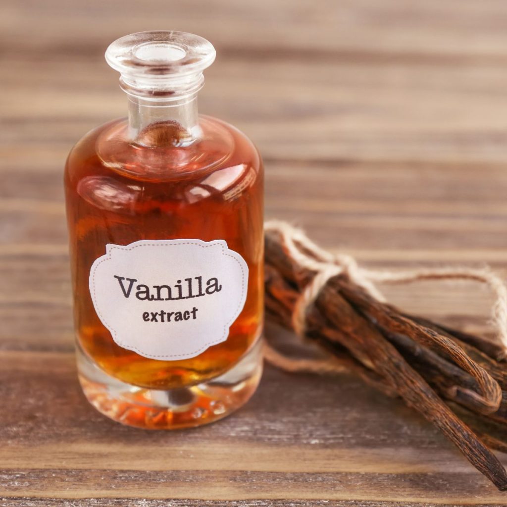 A bottle of vanilla extract rests on a wooden table with a set of vanilla beans.