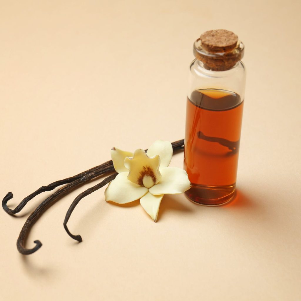 A small bottle of vanilla extract rests on a table with a set of vanilla beans and a vanilla orchid.