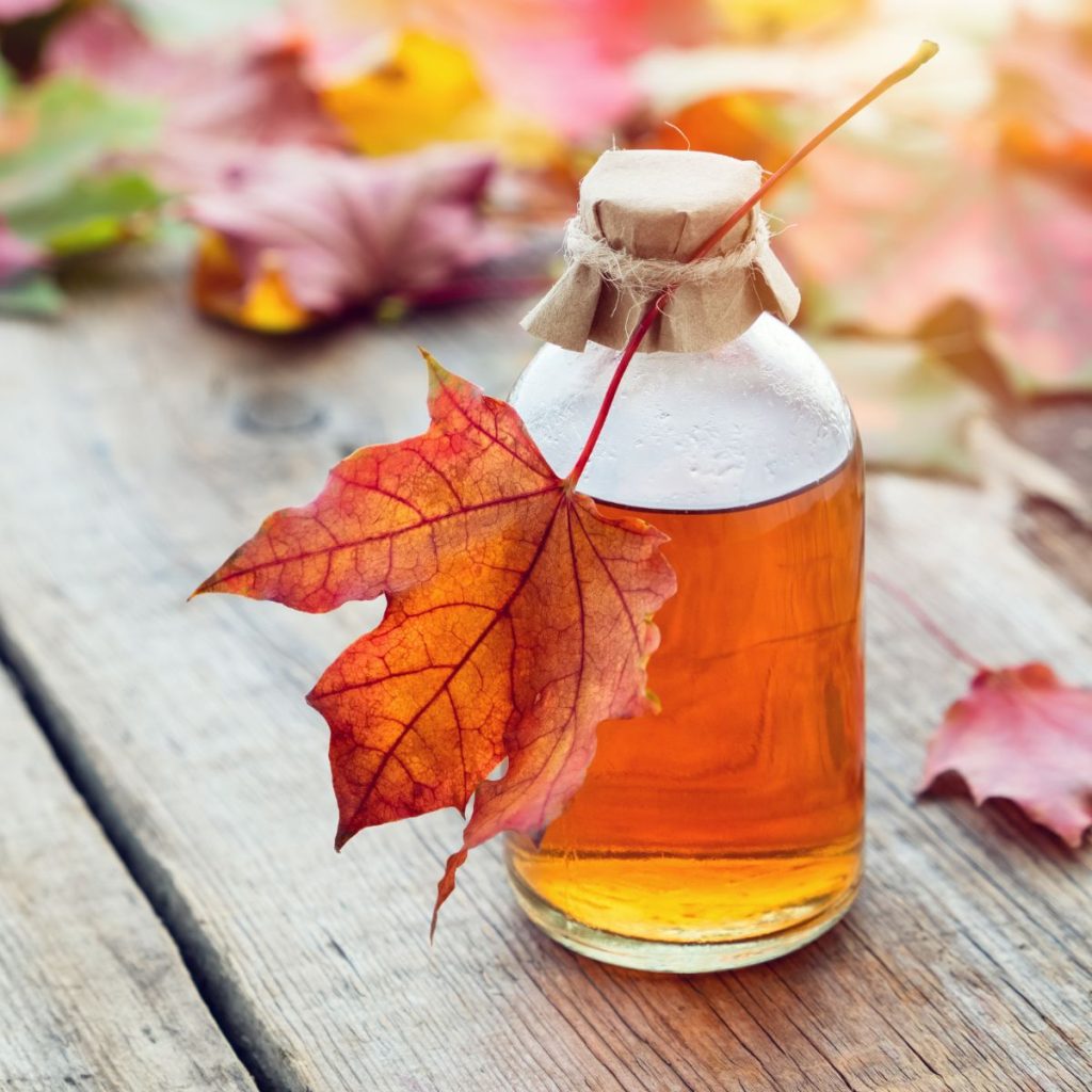 A bottle of maple syrup sits on a wooden table.