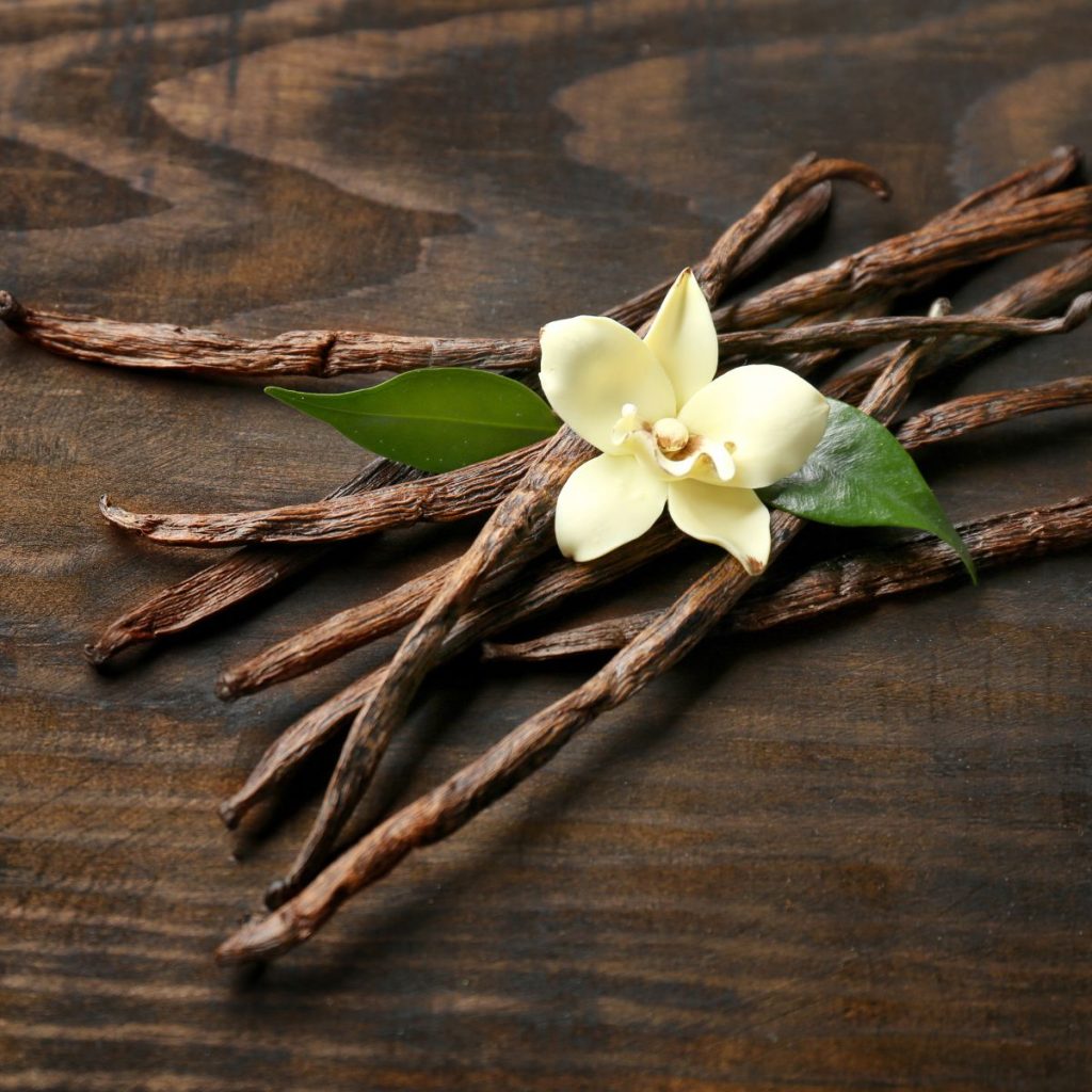 A couple of pieces of vanilla beans rest on a wooden table.