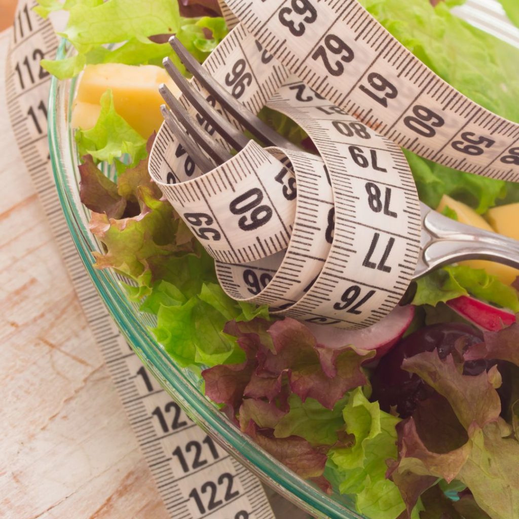 A measuring tape and fork rests on top of a salad.