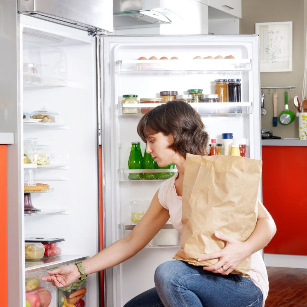 A woman organizes her groceries in the refrigerator.