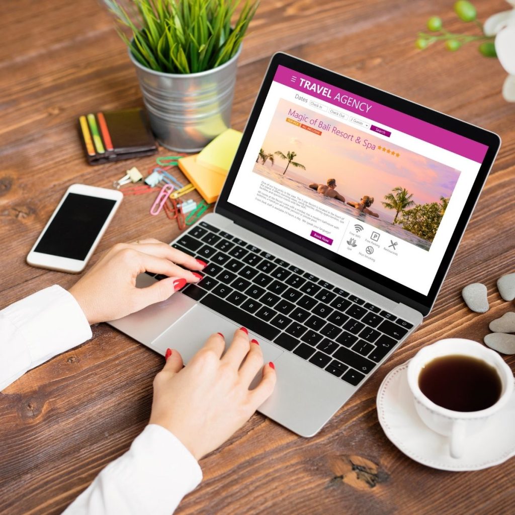 A pair of hands rests on a laptop while searching for travel accommodation online.