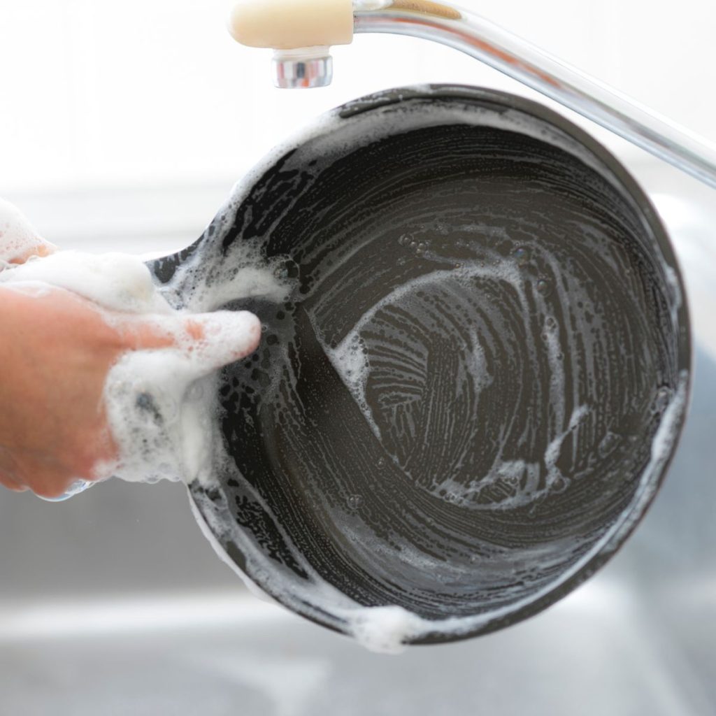 A steel pan is being hand-washed, showing one of the best ways to clean All-Clad pans.