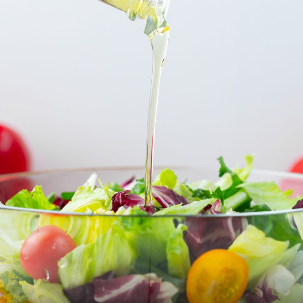 Extra virgin olive oil gets poured into a transparent salad bowl.