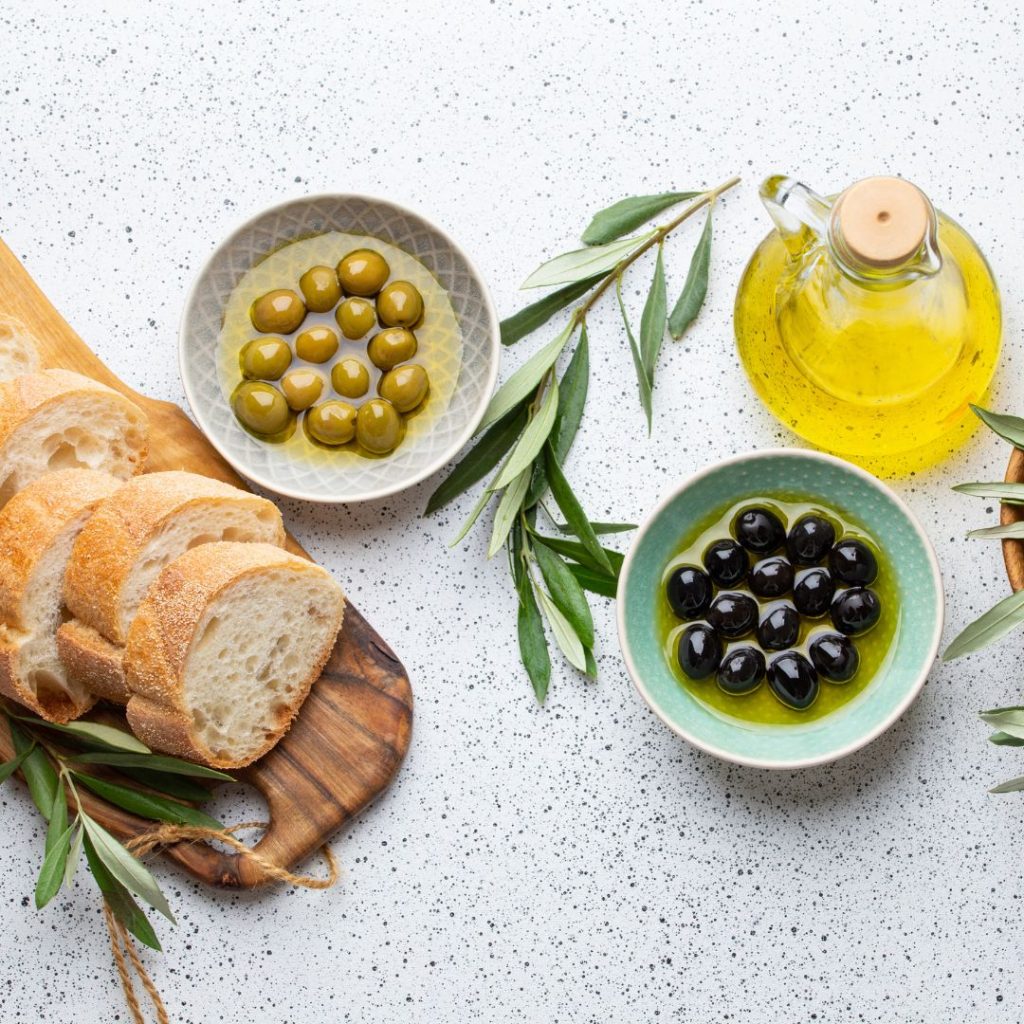 Olives, olive oil, and bread rest on a marble-textured table.