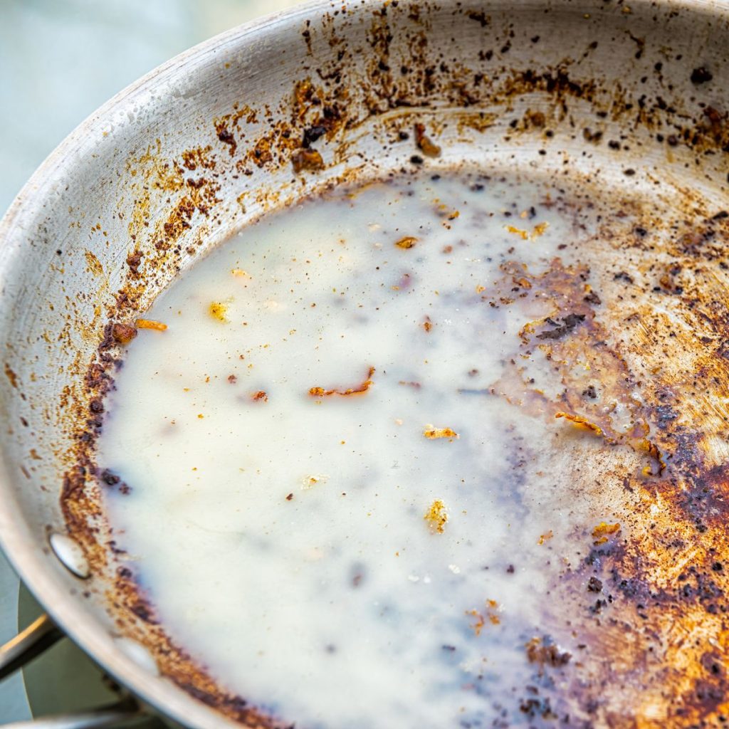 A cooking pan with stubborn stains gets washed with soap.