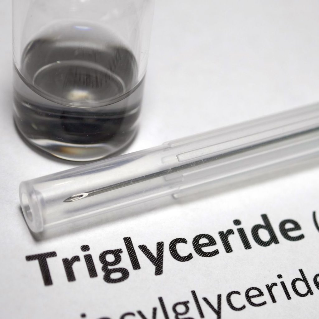 A needle and a bottled liquid rest on top of a paper with the word "triglyceride" imprinted on it.