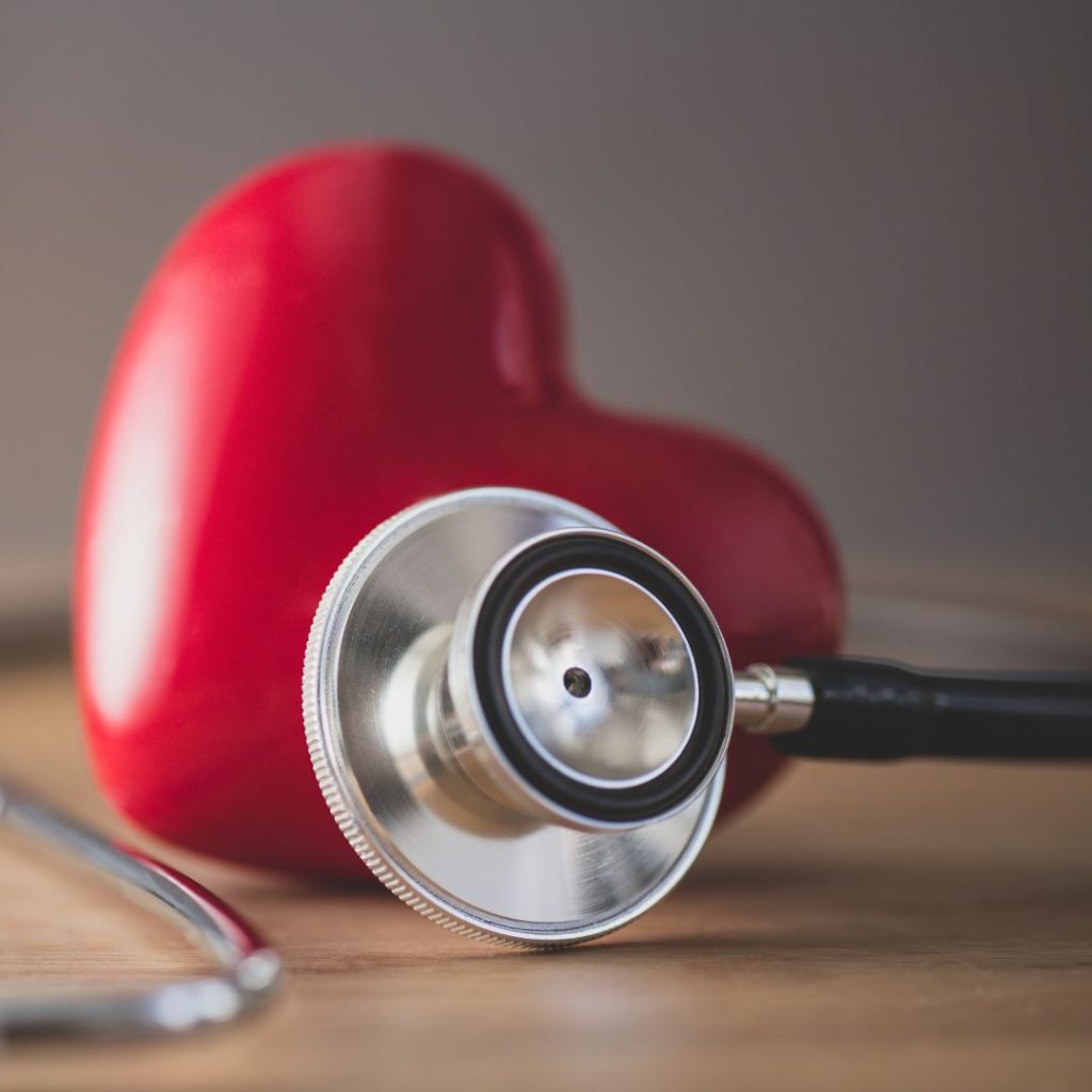 A stethoscope rests on a table with a solid heart figure.