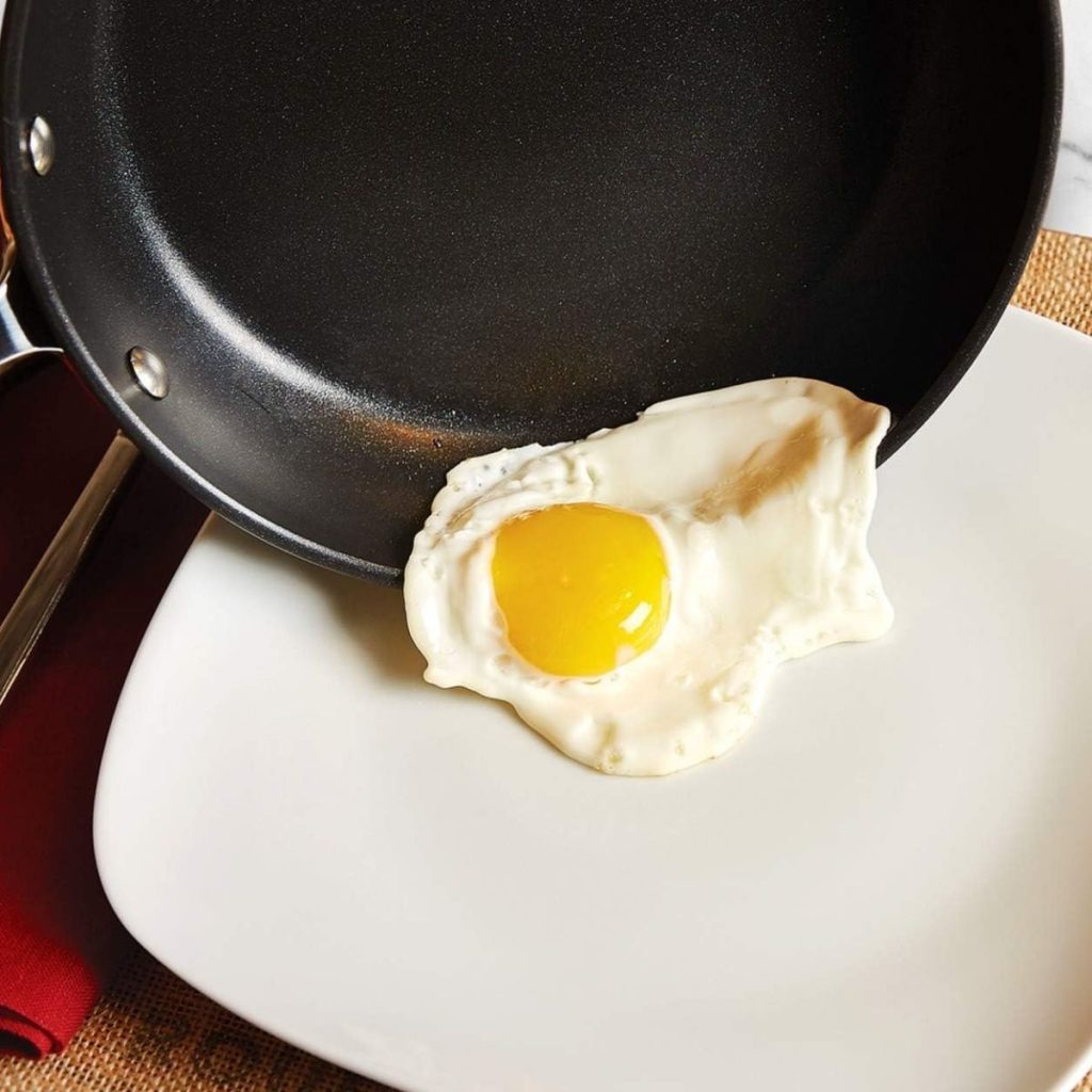 An egg is transferred from an All-Clad Hard Anodized pan to a white plate. (Photo courtesy of Amazon)