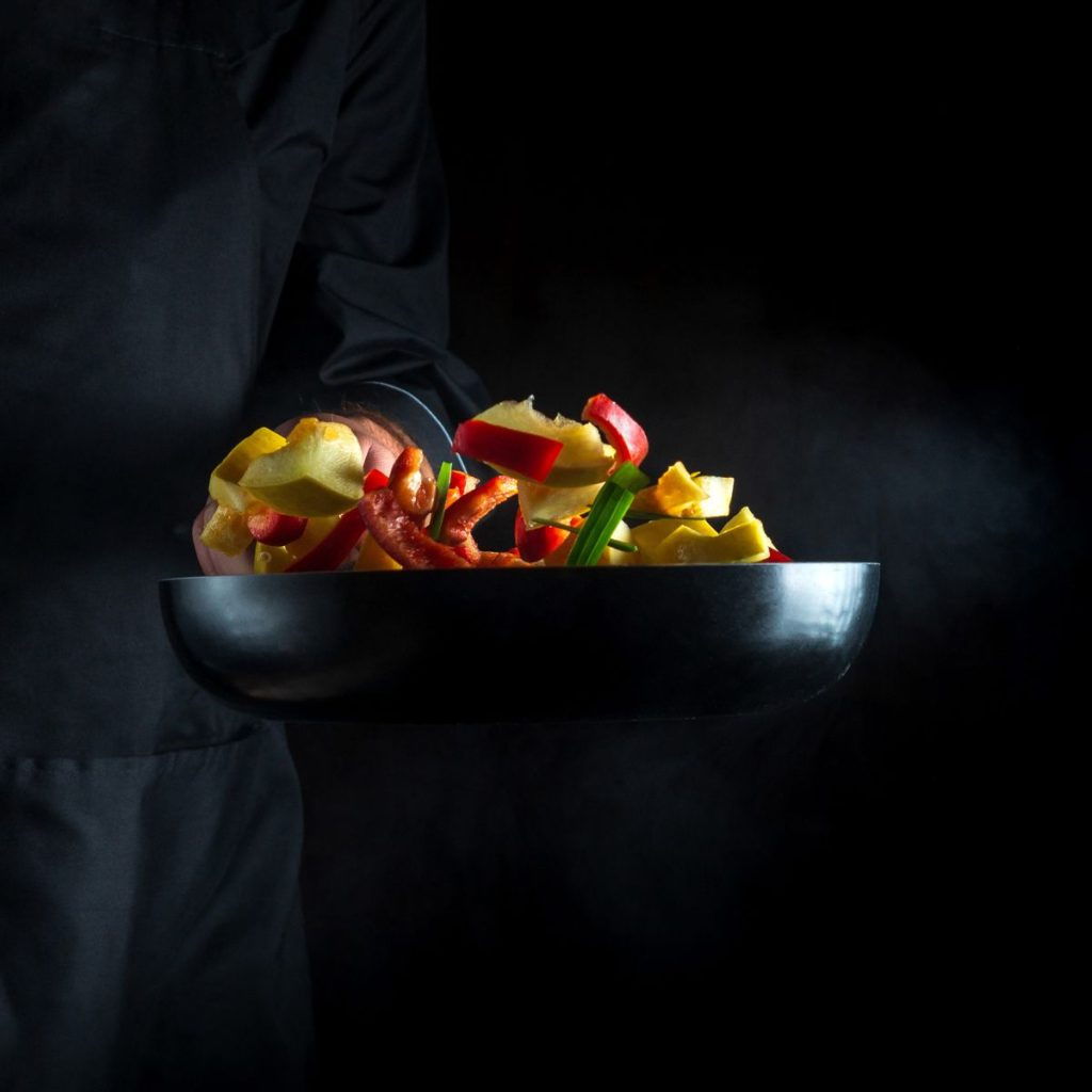 A chef tosses multiple vegetables with a cooking pan.