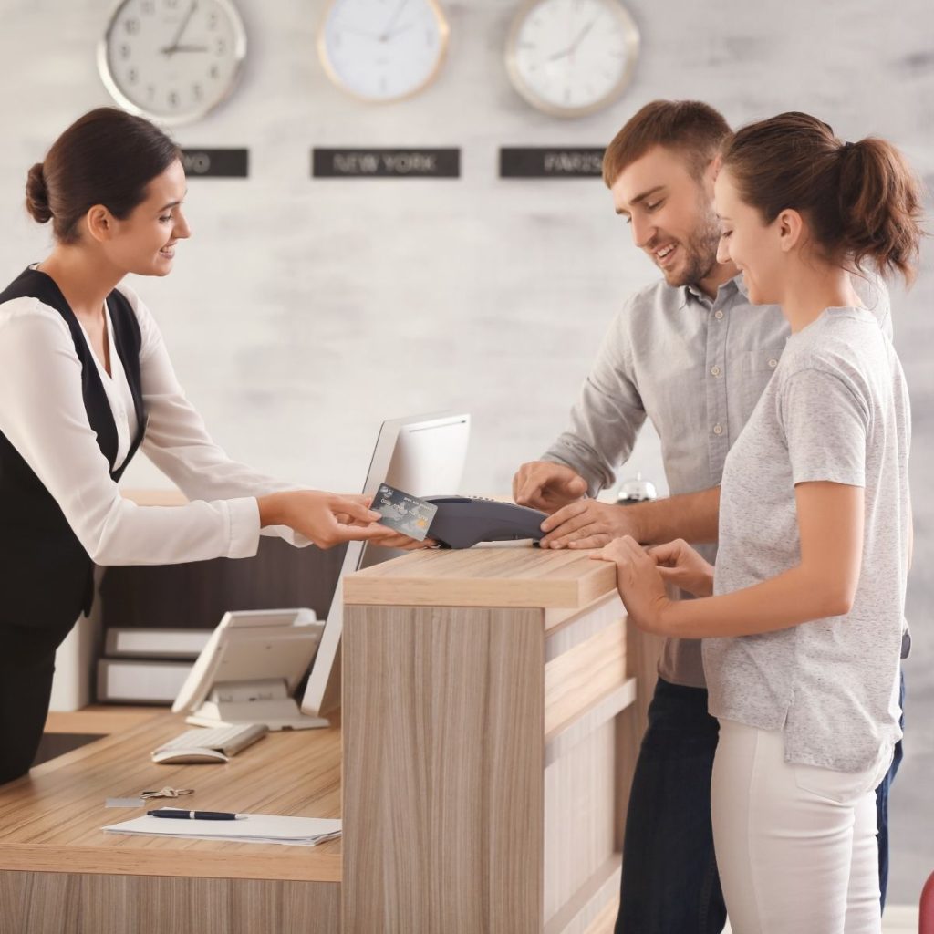 A couple talks to a hotel receptionist while booking their room. (ADIE Article: Booking.com vs. Tripadvisor)