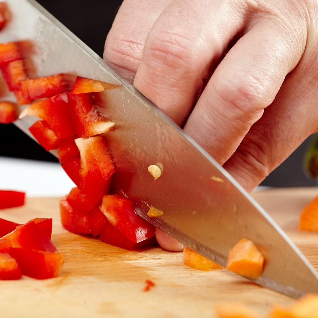 A knife cuts a bell pepper on a chopping board.