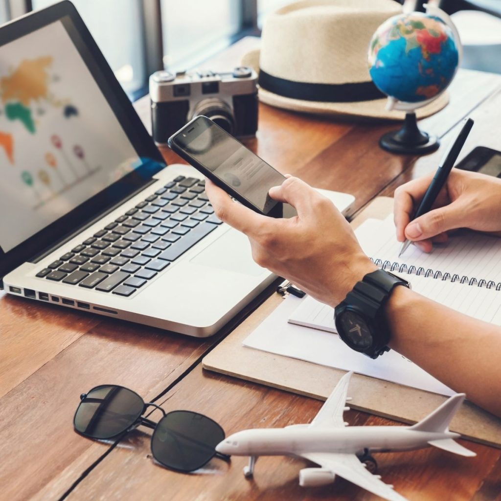 A human books an international trip using his phone and laptop.