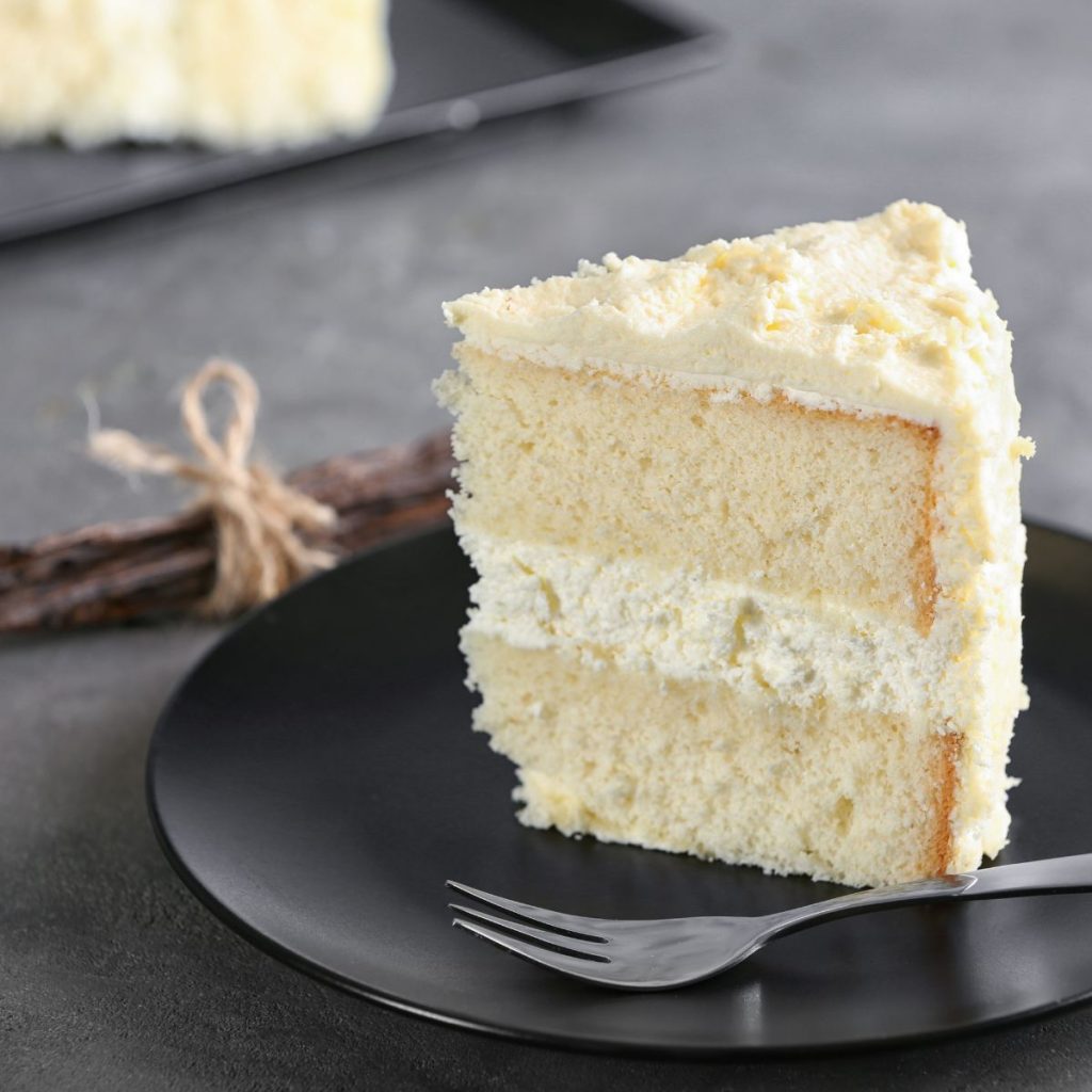 A plate of vanilla cake rests on a table with some vanilla beans.