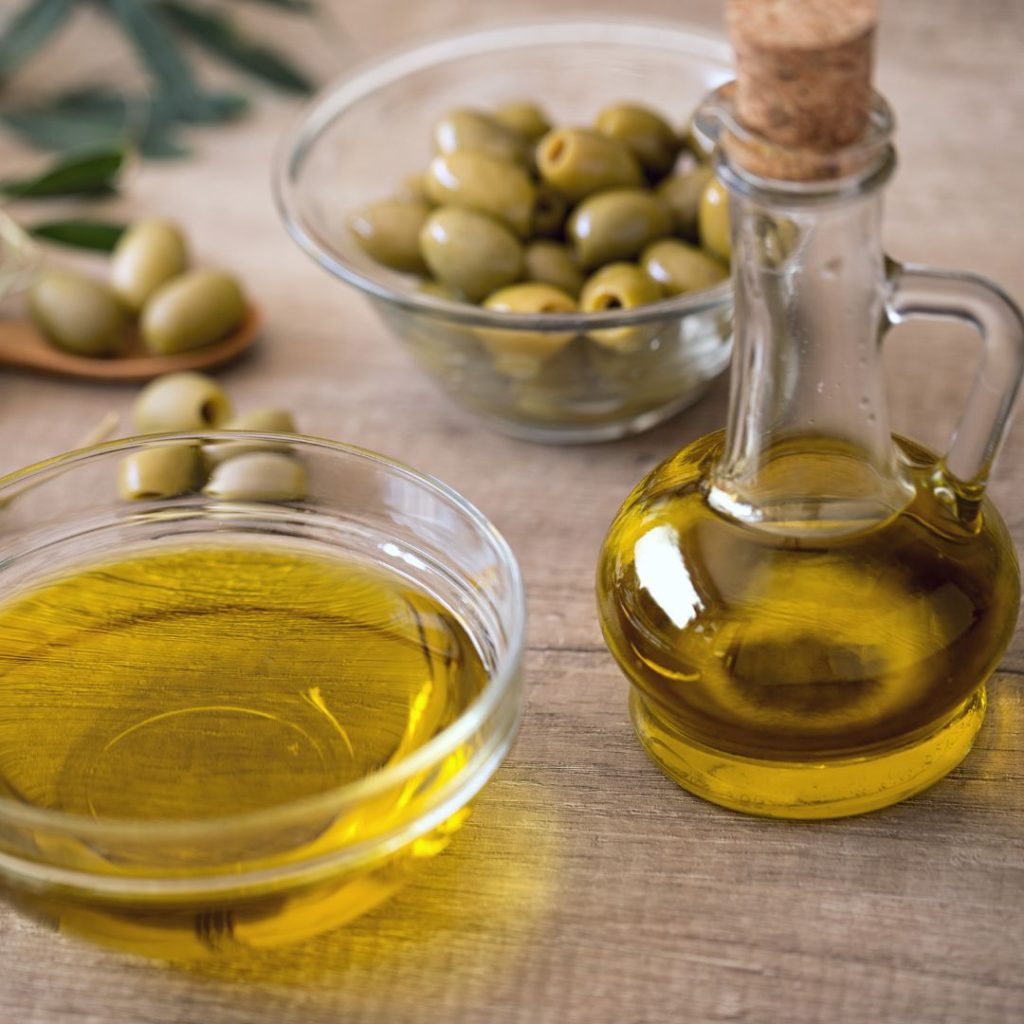 Containers of extra virgin olive oil rest on a table with a bowl of olives.