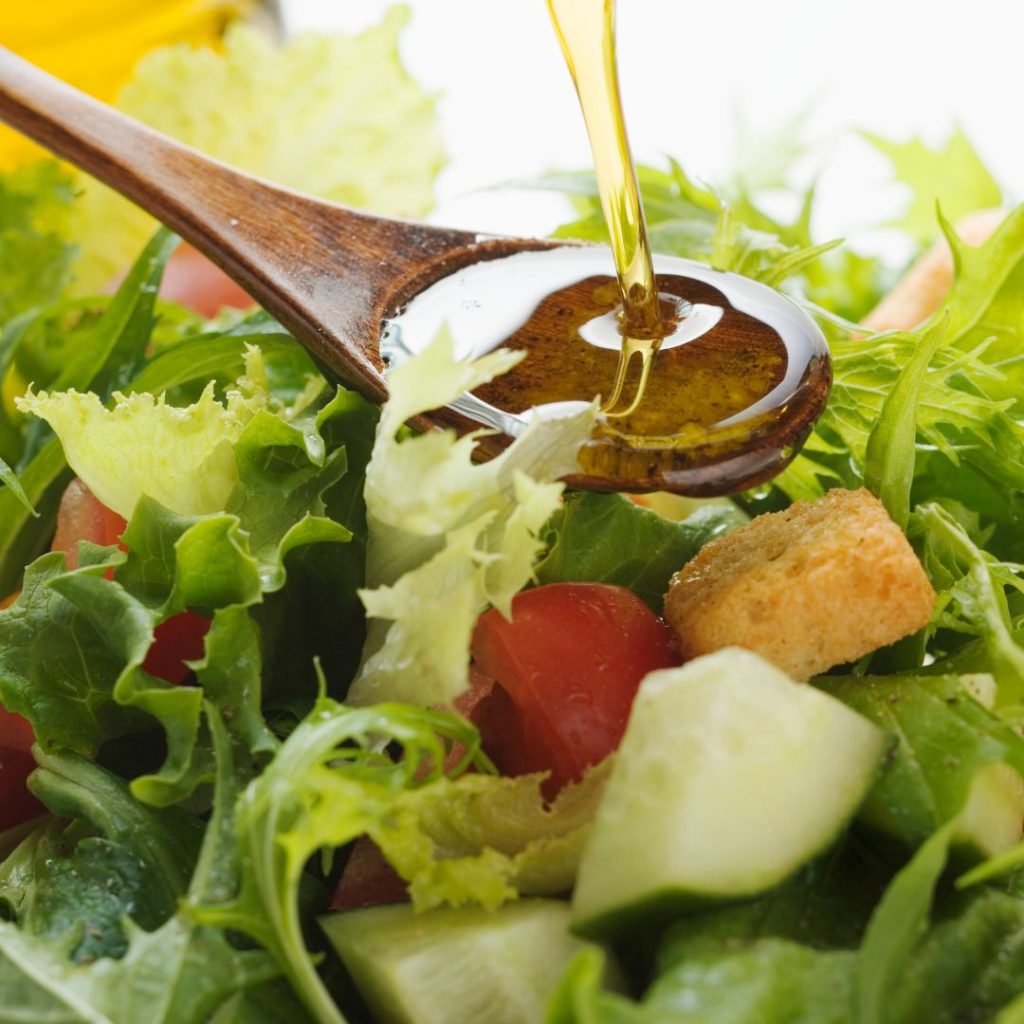 Extra virgin olive oil gets poured on a wooden spoon before drizzling into a salad bowl.