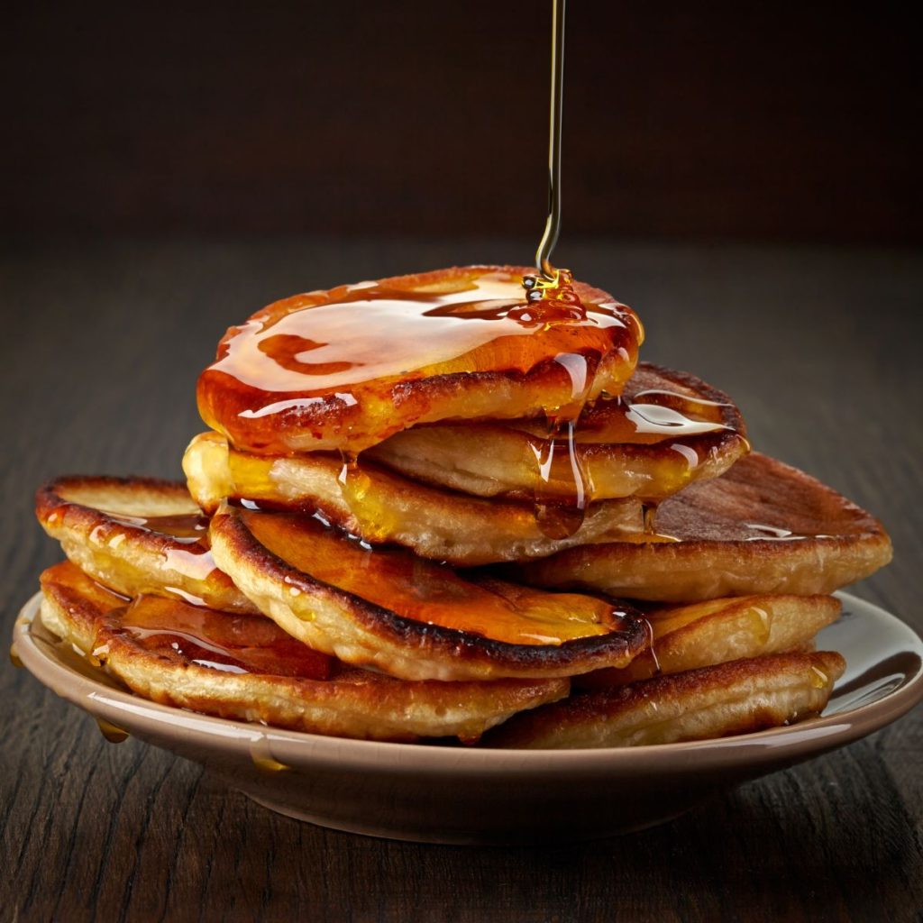 Maple syrup is poured on a pancake stack on a plate.