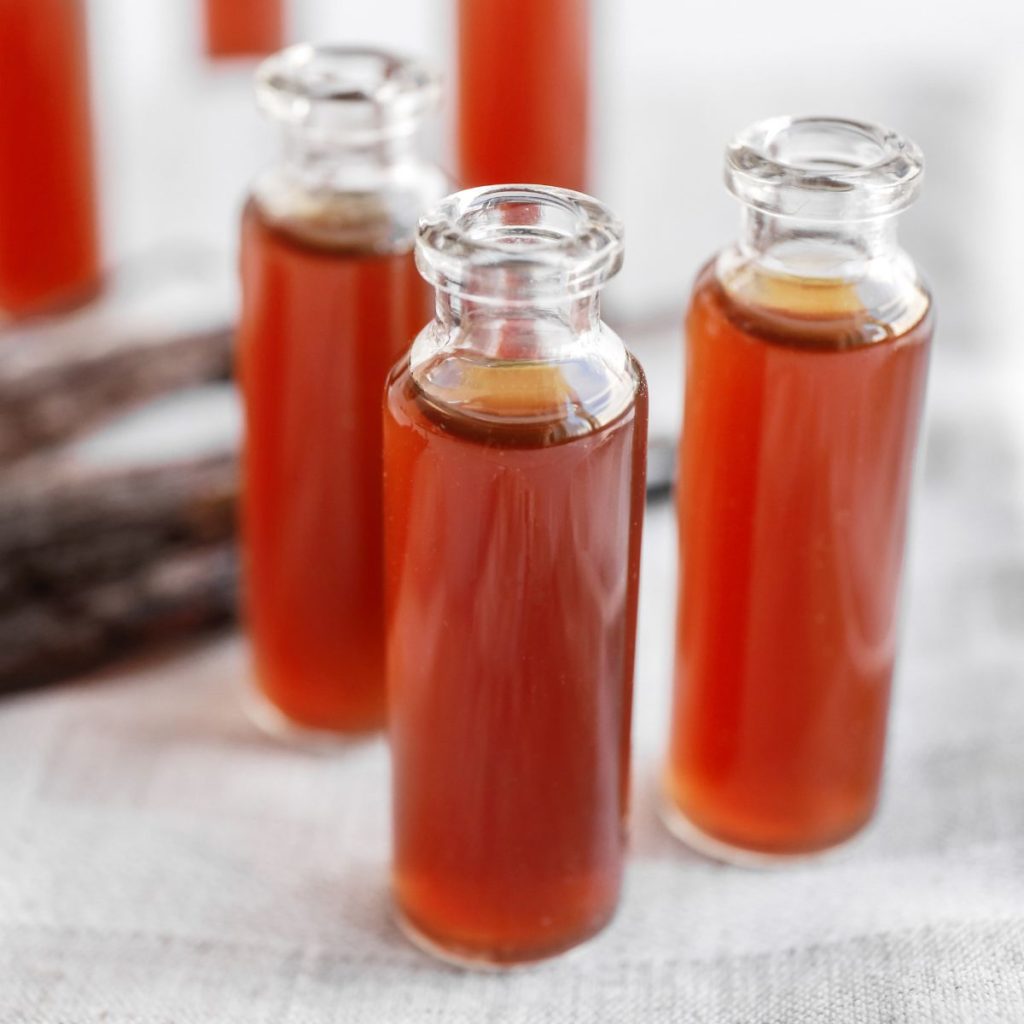 Three miniature bottles of vanilla extract rest on a tablecloth.