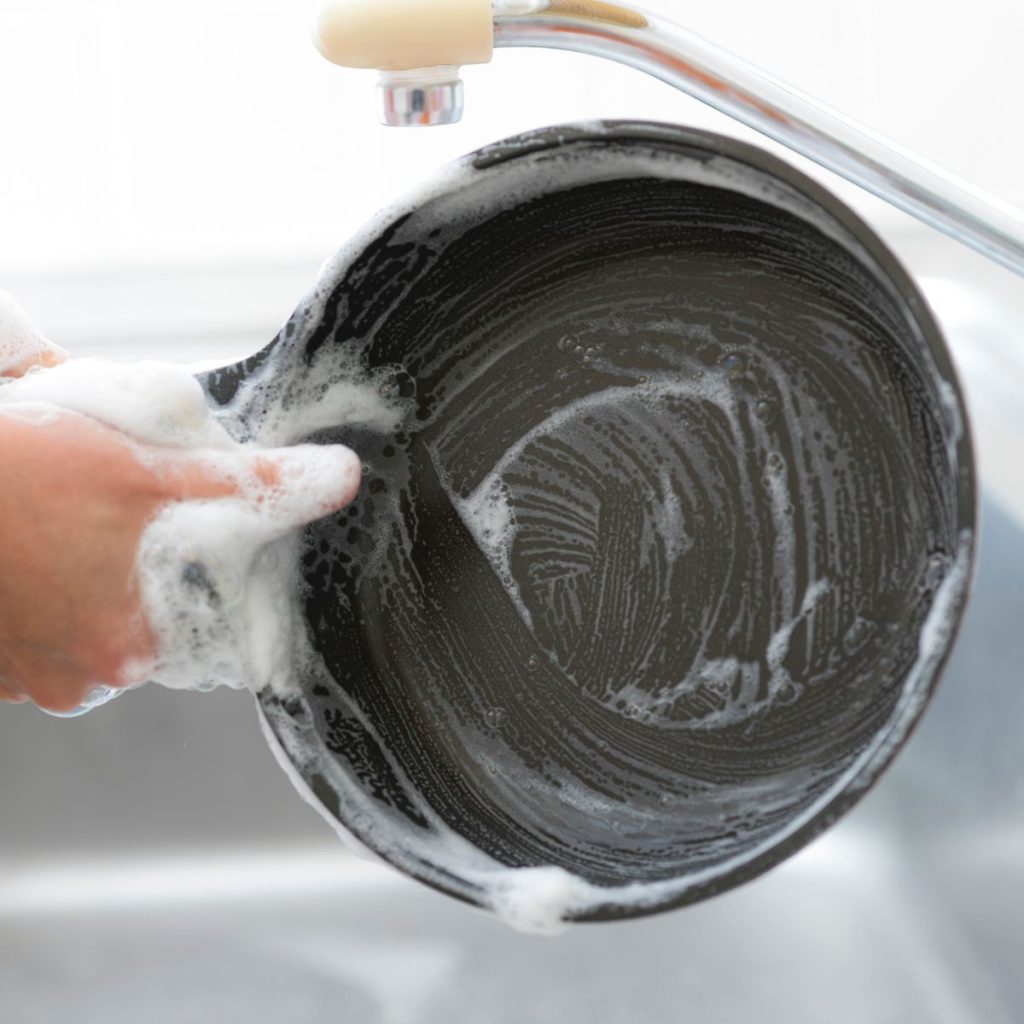 A human washes a non-stick pan with soap.