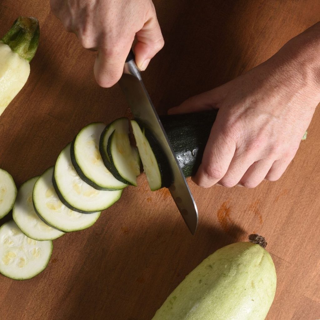 A knife cuts a cucumber on a chopping board.