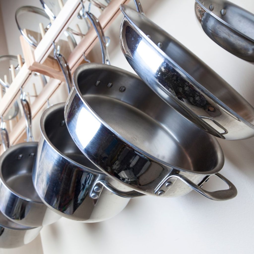 A set of steel pans are hung on a kitchen rack.