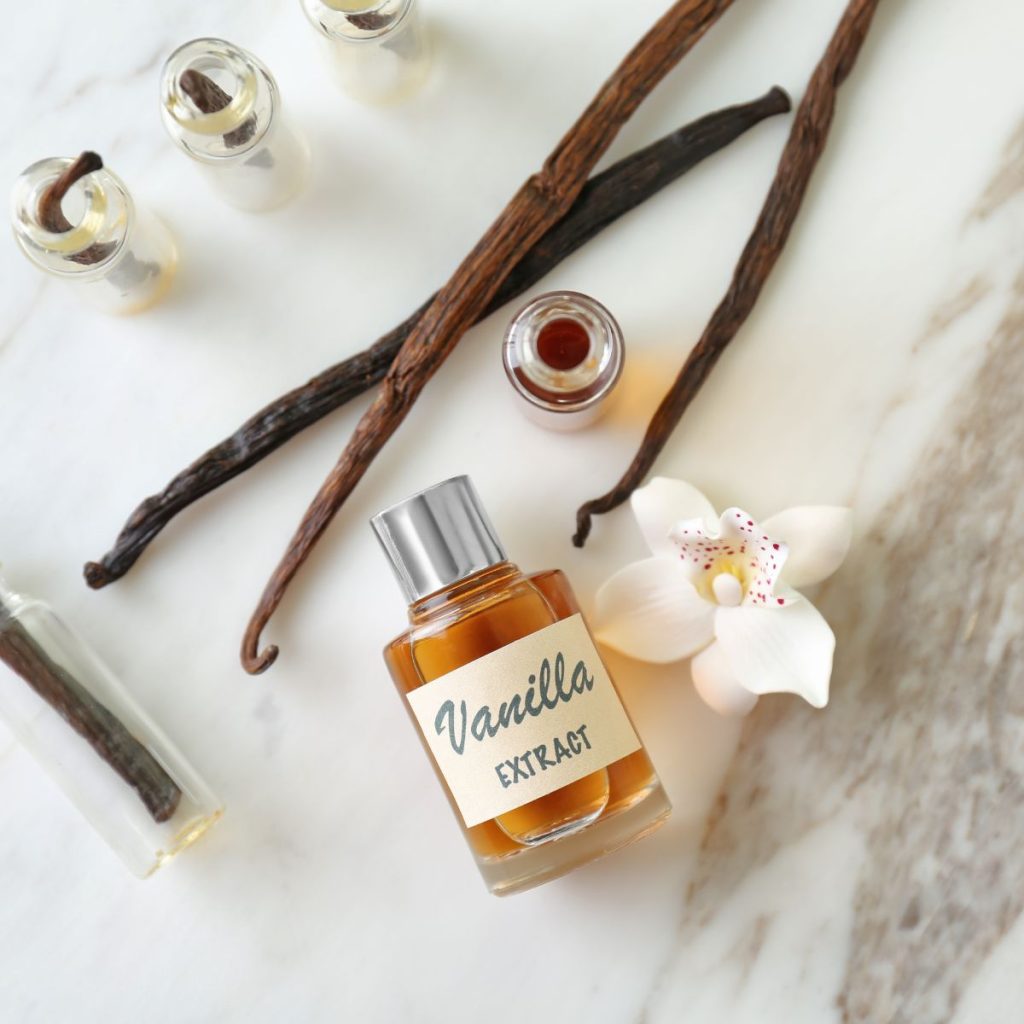 A sophisticated bottle of vanilla extract rests on a table with some vanilla beans and vanilla orchids.