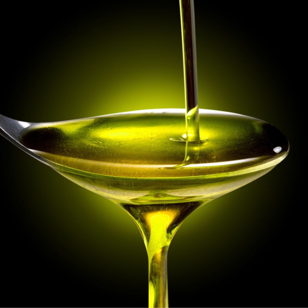 A spoon overflows with extra virgin olive oil.