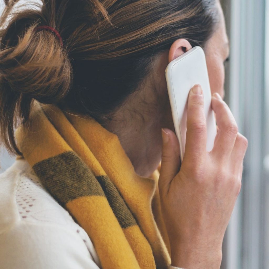 A woman places her phone close to her ear as she answers a phone call.