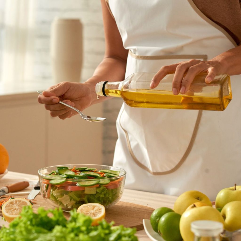 A woman pours extra virgin olive oil into a salad bowl.