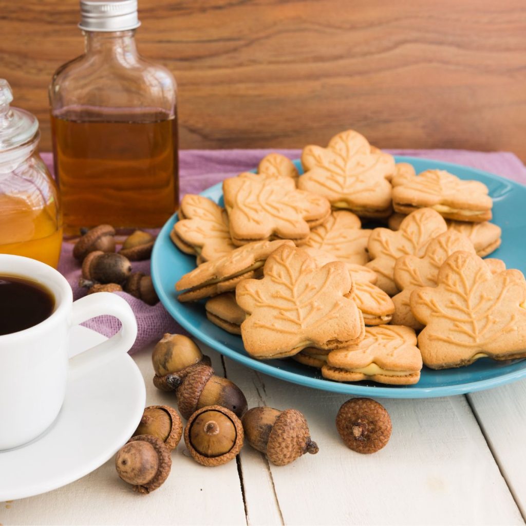 Vanilla extract, maple syrup, and a plate of maple-shaped cookies rest on a wooden table.