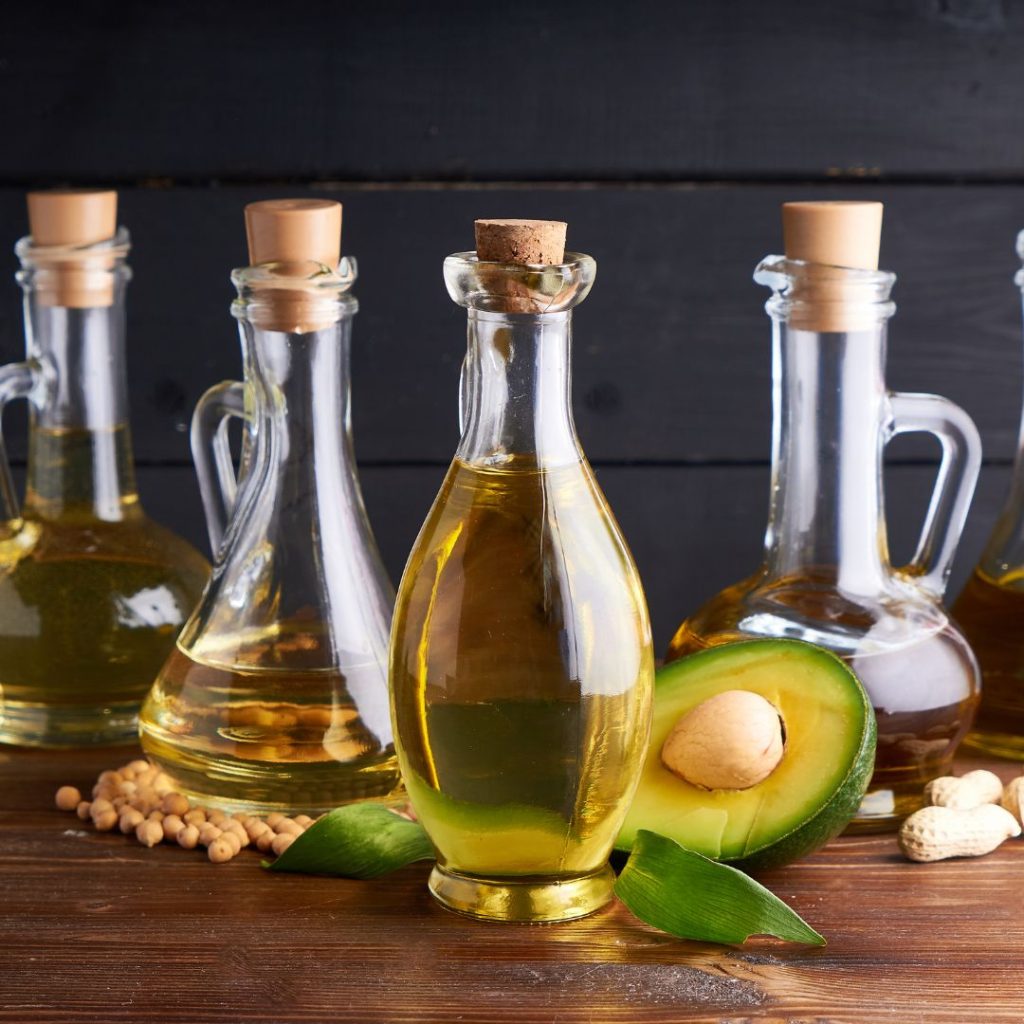 Various cooking oils rest on a wooden table with their fruit and vegetable sources.