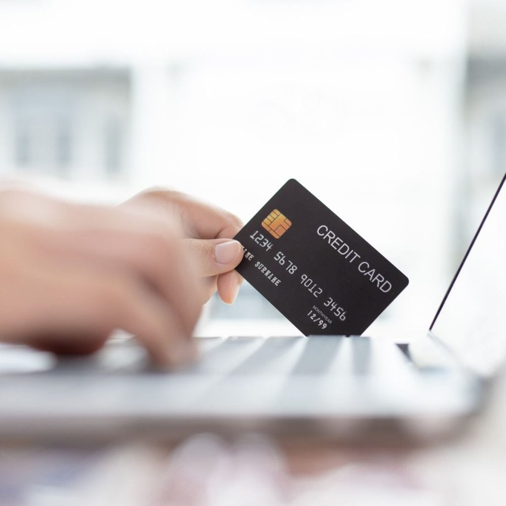 A credit card is held next to a computer.