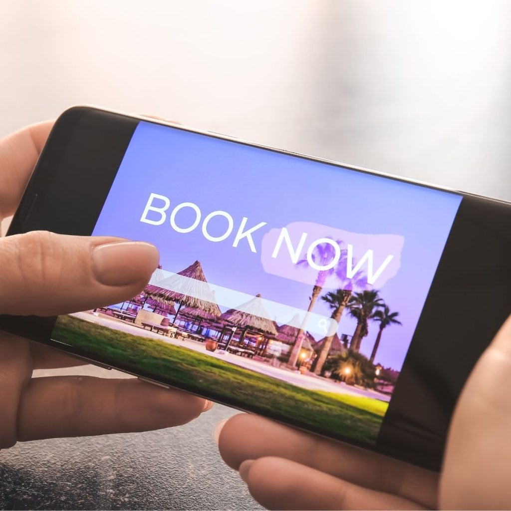 A pair of hands hold a phone that shows a graphic with a call to action that encourages buyers to book hotels now.