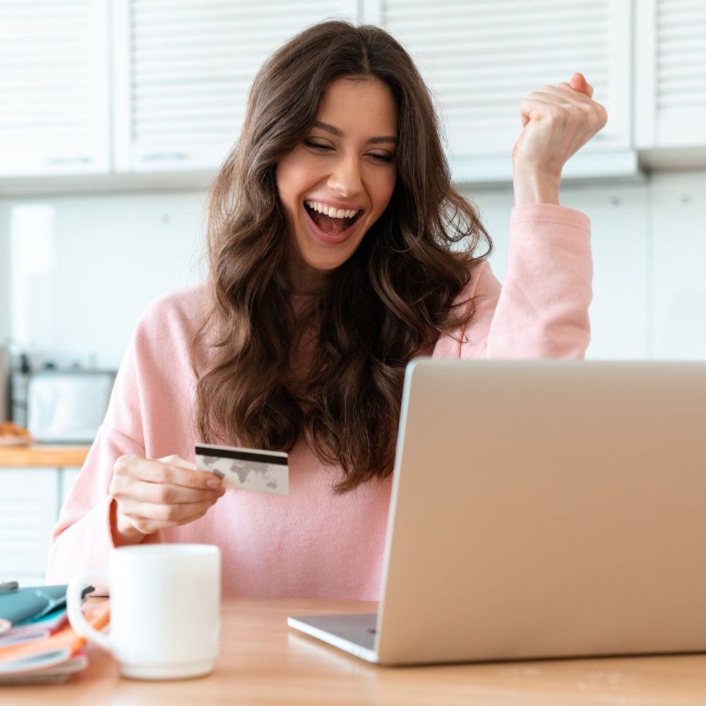 A happy woman looking at a laptop while holding a credit card