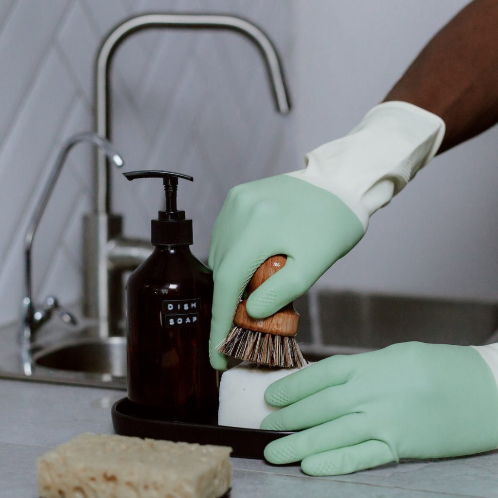 A person holding a brush with a mild dish soap and other cleaning materials at the side