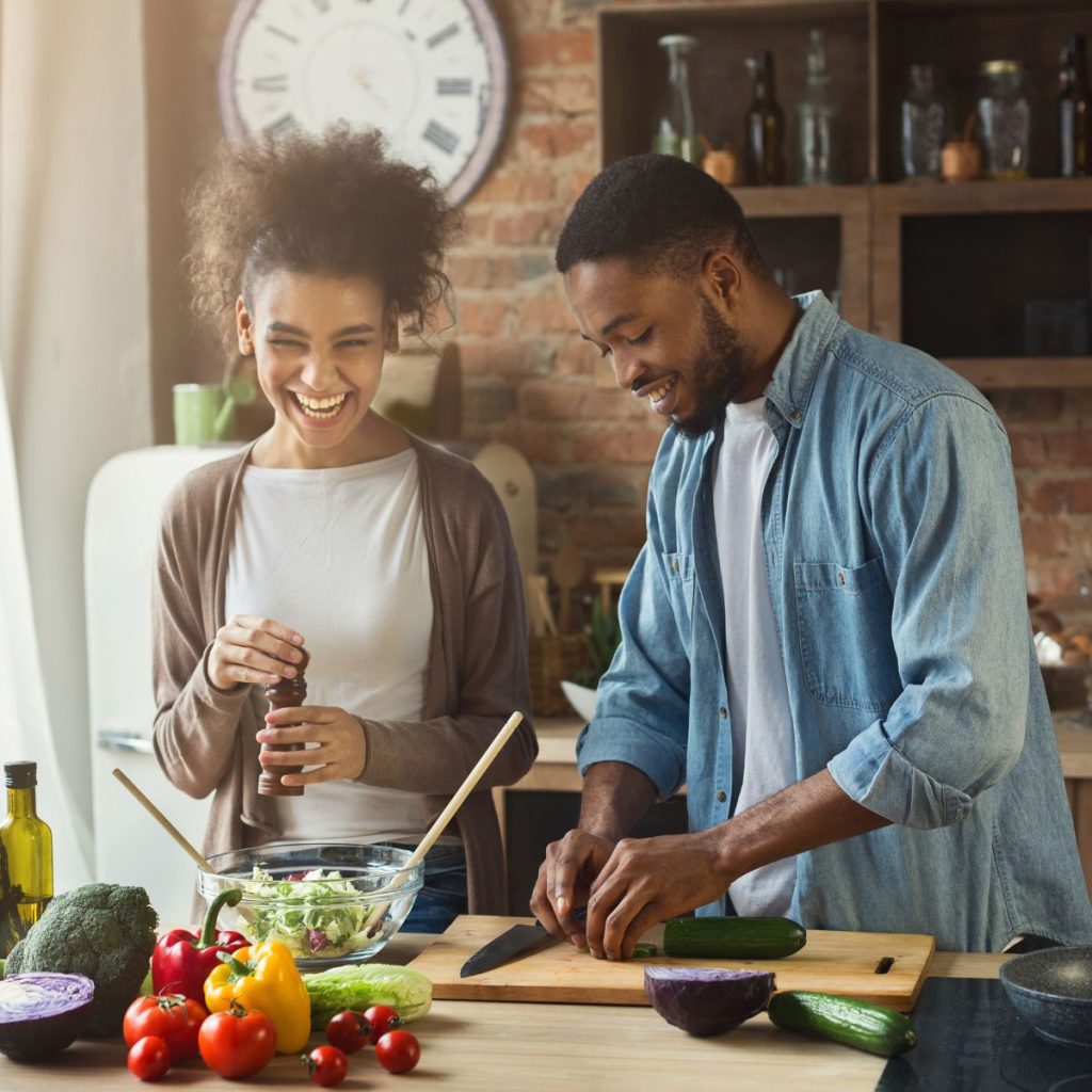 A smiling couple preparing a salad with the use of a bamboo utensil