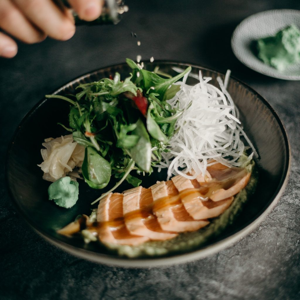 Adding black sesame seeds into a bowl with vegetables and sliced meat